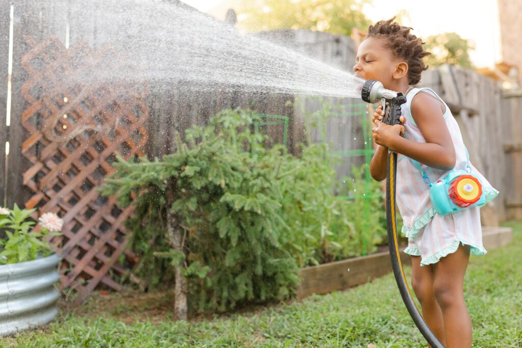 A little girl drinks from a water hose in a backyard Lexington KY garden during a family photo session.
