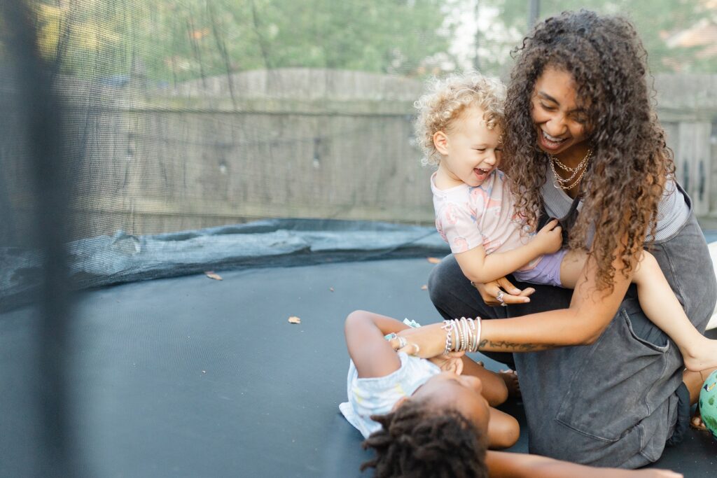 A mom tickles her daughters on a trampoline during their family photo session in Lexington KY. 