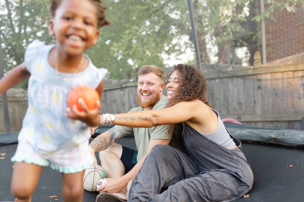 A mom and dad laugh as they play with their daughters on a trampoline at their in home family session in Lexington KY.