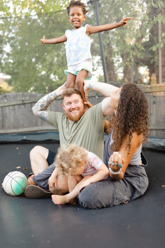 A mom and dad play with their two daughters on their trampoline during their family photo session in Lexington KY. 