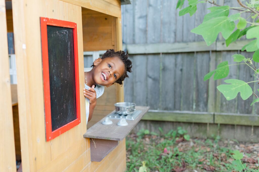 A little girl plays in her backyard playhouse during a family photo session in Lexington KY.
