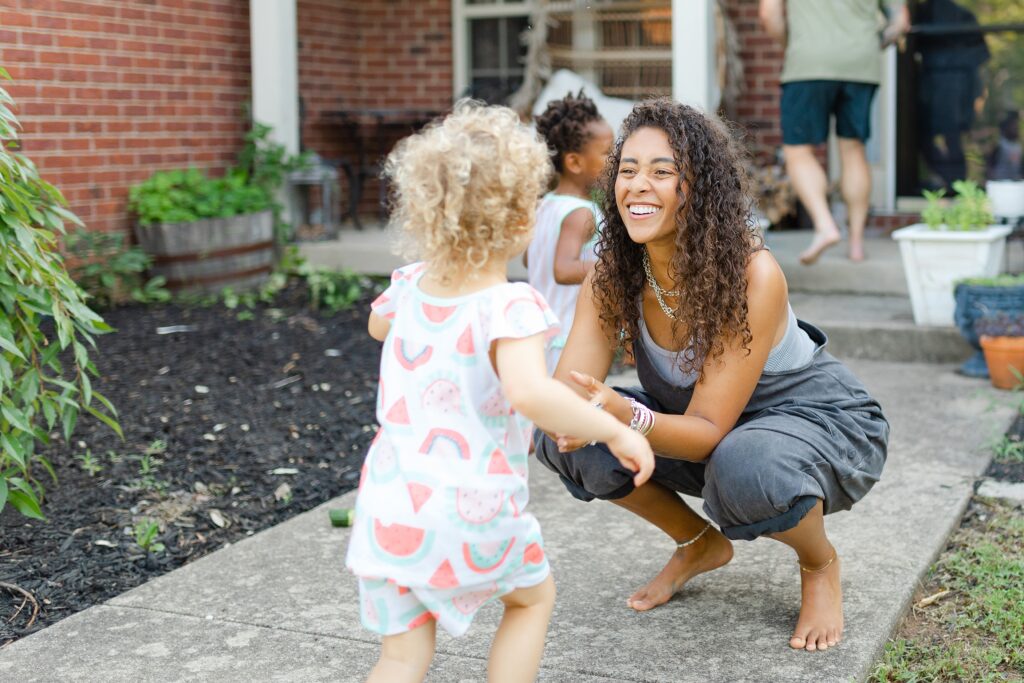 A curly-haired little girl runs to her mom as her mom joyfully welcomes her.