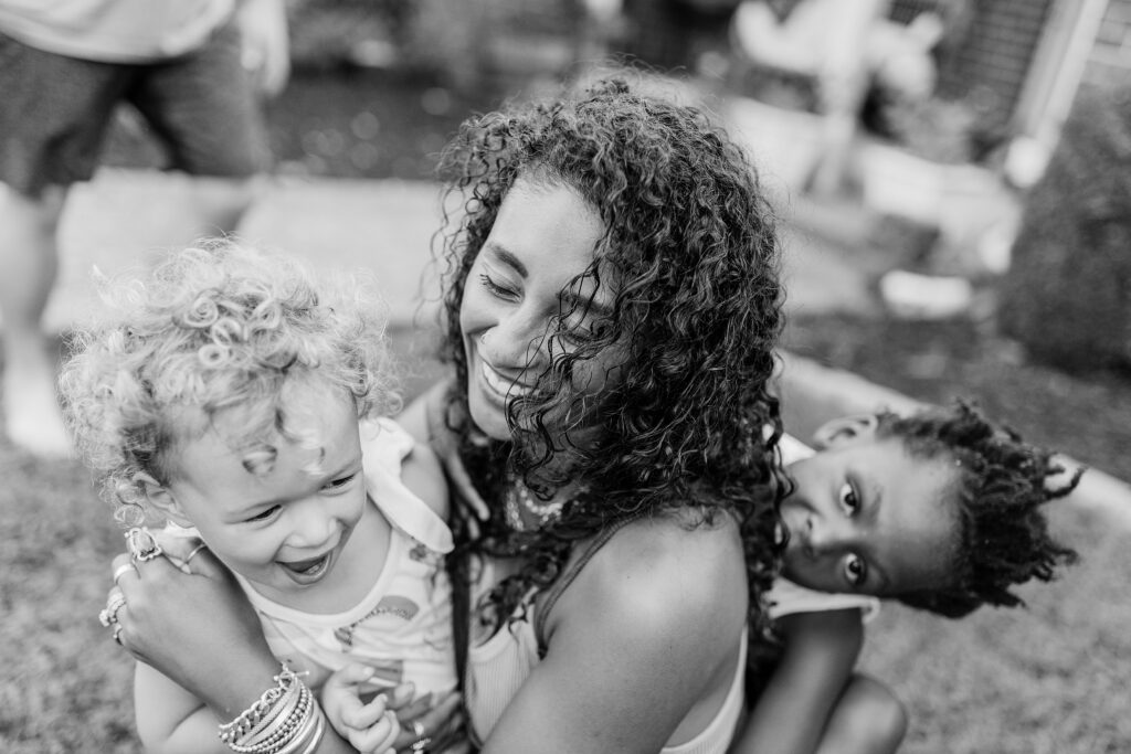 A black and white image of sisters playing with their mom during a family photography session.