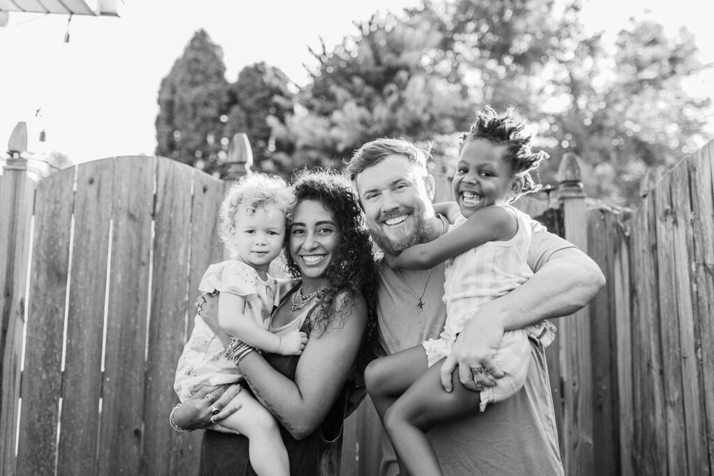 A black and white image of a family of four with two sisters snuggling up to their parents during the lifestyle family session in Lexington KY.