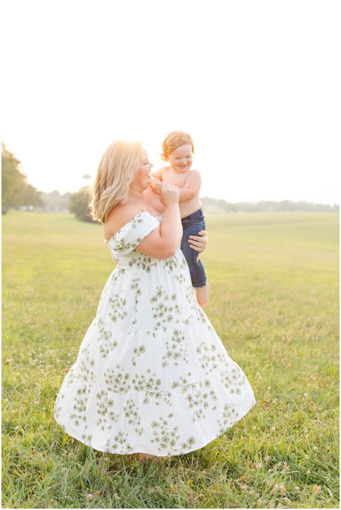 A mom dancing with her toddler son while her dress twirls in a field at sunset at Keeneland in Lexington KY.