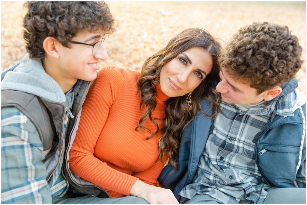 A mom sits with her two teenage sons while they hug her.