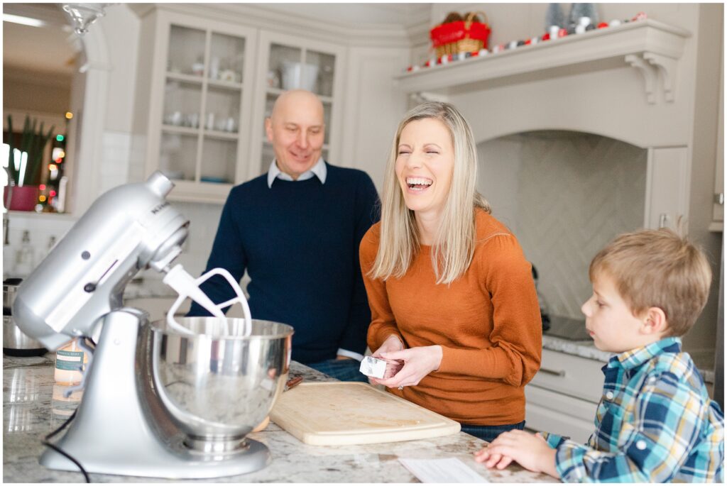 A mom laughing with her husband and son as they make Christmas cookies during their family photography session with Priscilla Baierlein.